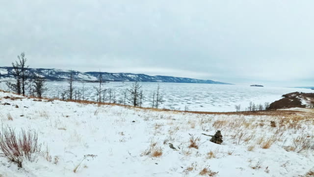 Travel-of-woman-on-ice-of-Lake-Baikal.-Pov-view.-Close-unique-buddhist-stupa-burkhan-monument-symbol-mystical-historic-ritual-island-Ogoi-landscape-mountains-shamanic-worship.-Trip-to-winter-island.