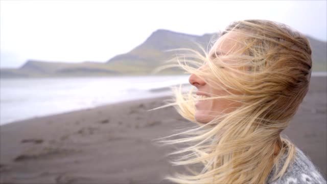 Junge-Frau-Betrachtung-stehenden-Meer-am-schwarzen-Sandstrand,-Haare-im-Wind-Island-Slow-Motion-Video-Menschen-reisen-Natur-Konzept