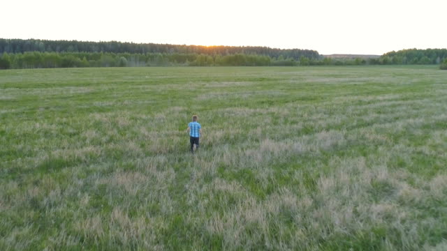Boy-is-running-down-the-field-on-sunset.-Back-view.