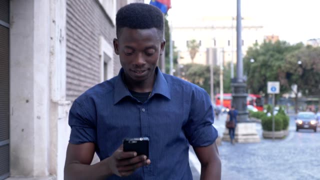 Retrato-del-negro-africano-hombre-atractivo-pasear-por-la-ciudad,-escribiendo-en-su-smartphone