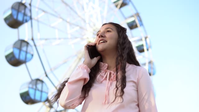 The-girl-is-talking-on-the-phone-standing-near-the-Ferris-wheel-.4K