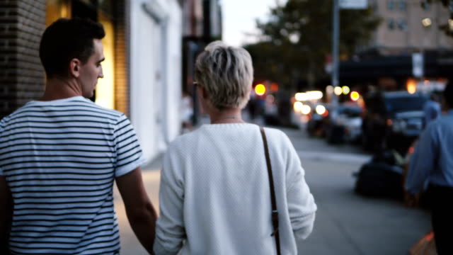 Happy-young-romantic-couple-hold-hands-walking-along-evening-Soho,-New-York,-blurred-street-lights-in-the-background