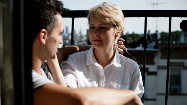 Beautiful-young-European-woman-talking-to-man.-Couple-sitting-at-a-small-sunny-apartment-balcony-talking-to-each-other
