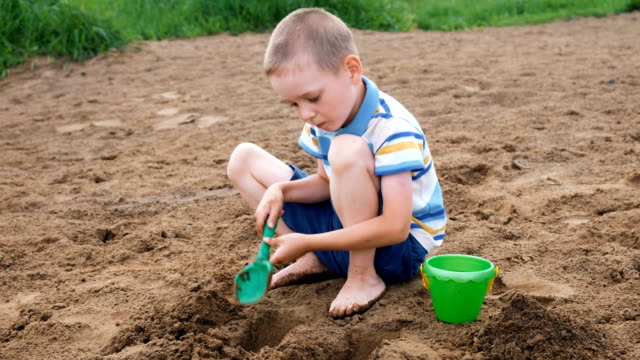 Serious-little-boy-digs-a-pit-with-a-shovel.-Kid-playing-on-the-beach