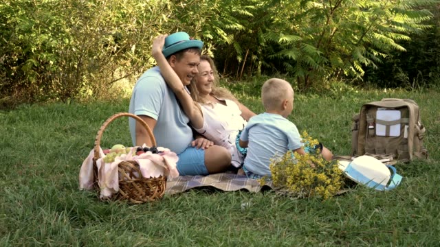 Mamá,-papá-y-pequeño-hijo-divirtiéndose-y-jugando-sombreros-sobre-la-hierba-en-el-parque.-Tenían-una-comida-campestre-al-aire-libre.-Proceso-de-cosecha.
