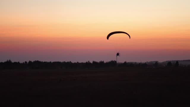 The-pilot-on-a-paraglider-flies-in-the-sky-after-sunset-with-orange-.-background