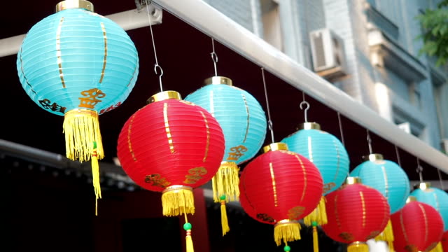 Chinese-lanterns-sway-in-the-wind-in-the-afternoon.-Oriental-paper-lights-of-red-and-blue-colors-are-swaying-with-the-wind-on-the-roof-of-a-building-by-day-on-the-street.