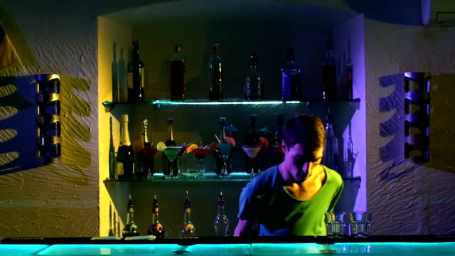 Young-bartender-making-tricks-with-two-glasses-and-bottle--standing-behind-the-bar,-slow-motion