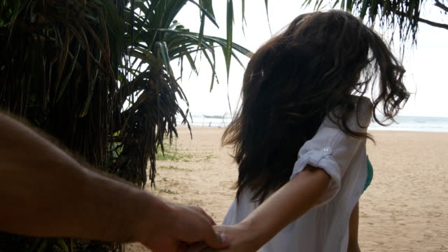 Girl-holding-male-hand-and-running-on-tropical-exotic-beach-to-the-ocean.-Follow-me-shot-of-young-woman-pull-her-boyfriend-on-the-sea-shore.-Summer-vacation-or-holiday.-Point-of-view-POV