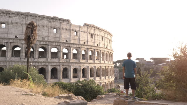 Mann-in-Sportbekleidung-steht-auf-einem-Hügel-vor-dem-Kolosseum-in-Rom-nach-der-Ausführung-bei-Sonnenuntergang-und-Überprüfung-Zeit-auf-seine-Uhr