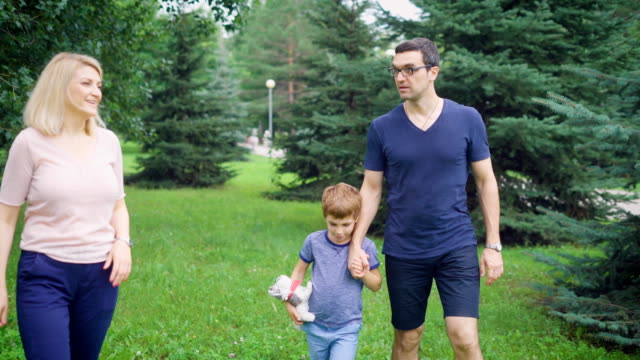 Los-padres-adultos-y-niño,-caminar-juntos-en-parque-verde