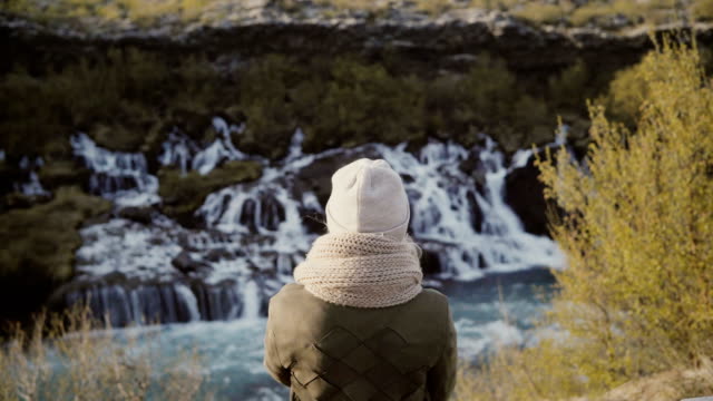 Back-view-of-young-woman-standing-in-mountain-valley-and-looking-on-waterfalls-in-Iceland,-exploring-the-nature