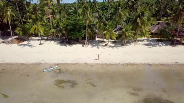 Drone-shot-aerial-view-of-young-man-arms-outstretched-relaxing-on-tropical-beach,-contemplating-nature.-4K-resolution-video-shot-in-the-Philippines,-Asia.-People-travel-vacations-concept