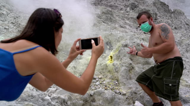 A-woman-is-taking-pictures-of-a-man-next-to-a-fumarole-on-a-smartphone