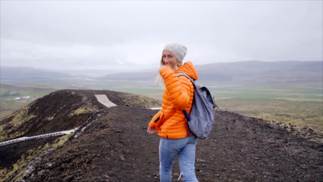 Slow-motion-Hiking-woman-gesturing-come-along-follow-me,-waving-and-hand-looking-at-camera,-Iceland