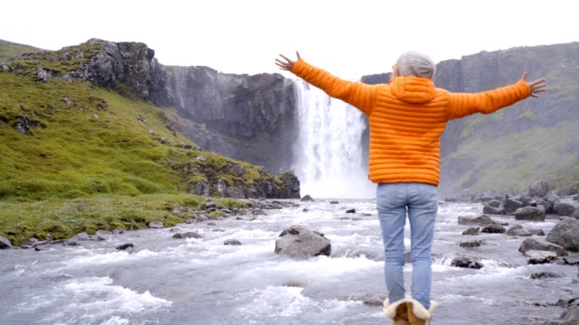 Junge-Frau-vor-dem-herrlichen-Wasserfall-in-Island-ausgestreckten-Armen,-fällt-Godafoss.-Die-Leute-reisen-Exploration-Konzept