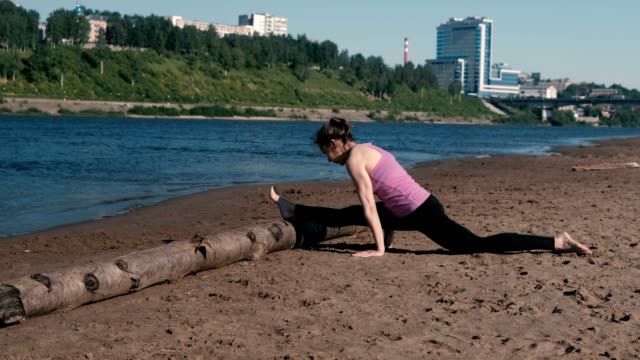 Woman-doing-stretching-sitting-on-twine-in-the-sandy-beach-at-sunset.-Beautiful-city-view.