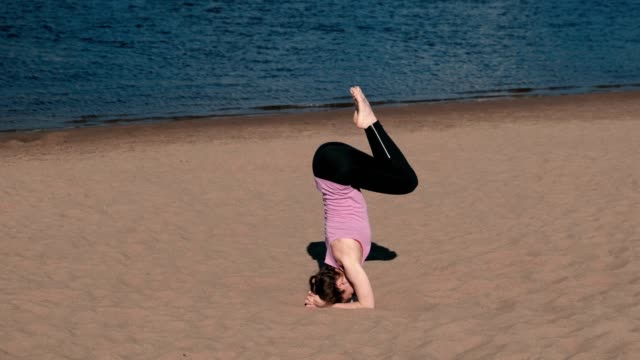 Mujer-haciendo-yoga-en-la-playa-por-el-río-en-la-ciudad.-Hermosa-vista.-Handstand.-La-guita-en-el-aire.