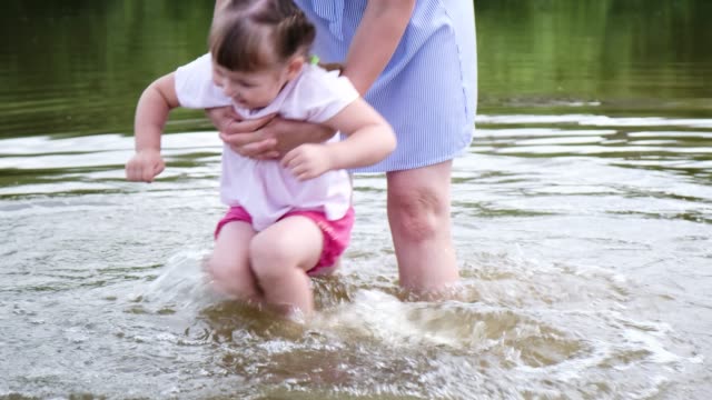 Mother-of-the-little-girl-washes-his-feet-in-the-river.-Woman-playing-with-her-baby-on-the-beach