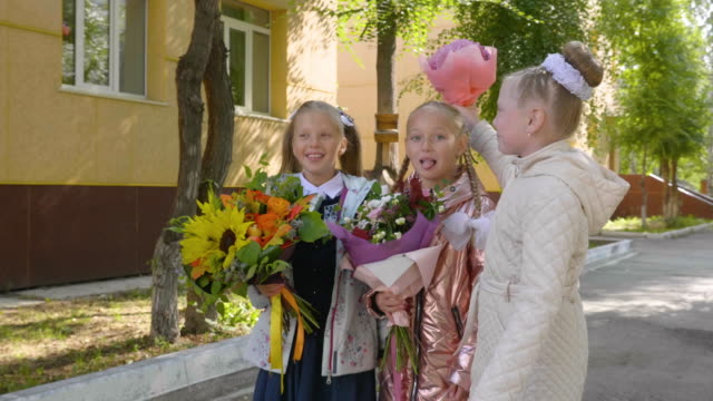 Verspielten-Schulmädchen-mit-Blumensträußen-lachen-und-Stand-in-der-Nähe-der-Schule