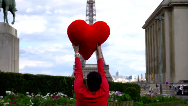 Mujer-joven-girando-alrededor-frente-a-torre-de-Eiffel-con-corazón-rojo-en-sus-manos-en-cámara-lenta-180-fps