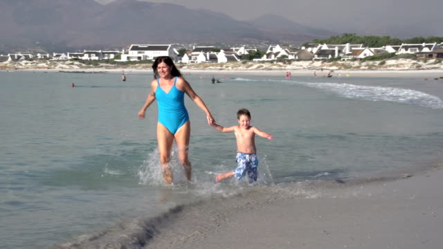 Mutter-und-junge-läuft-in-Richtung-Kamera-am-Strand,-Cape-Town