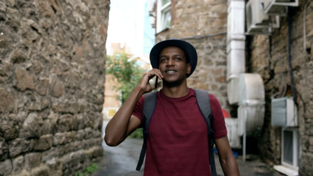 Toma-de-steadicam-de-turista-americano-africano-caminando-y-charlando-de-teléfono.-Joven-feliz,-viajar-por-Europa