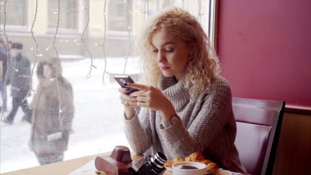 Joven-mujer-rizada-sentado-en-la-cafetería-con-teléfono