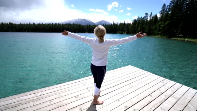 Young-woman-arms-outstretched-on-lake-pier,-Canada