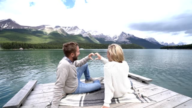 Young-couple-making-heart-shape-frame-on-mountain-lake-landscape,-Canada