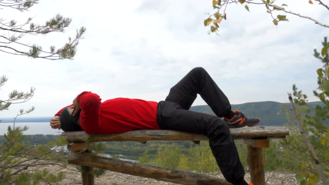 Tourist-man-He-is-lying-on-the-bench-in-the-mountains,-and-talking-on-the-phone-.--hiking.-a-tour-of-the-forest.-camping.-leisure.-ecotourism.-wild.-adventure-begins
