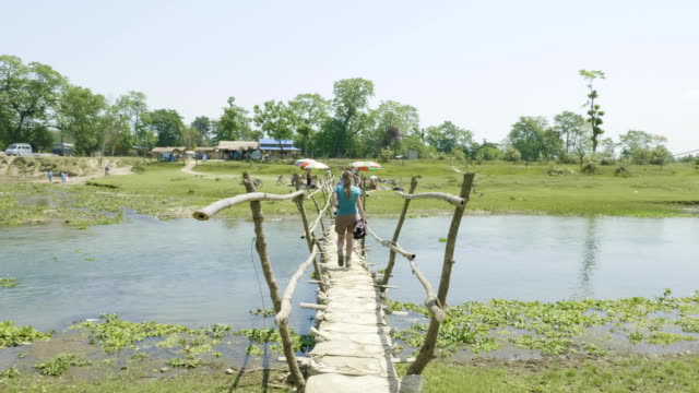 Girl-walks-along-the-wooden-bridge-through-the-river,-asia,-Nepal.