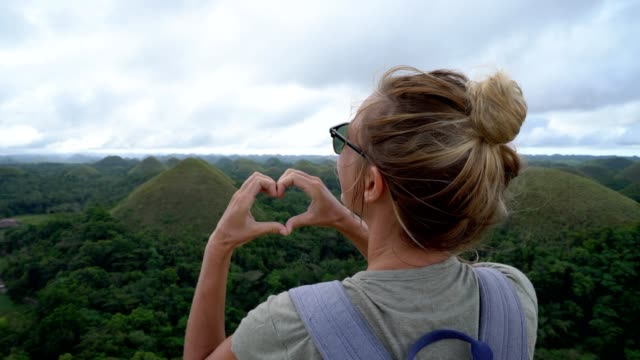 Girl-traveling-makes-heart-on-Chocolate-Hills-of-Bohol,-Philippines