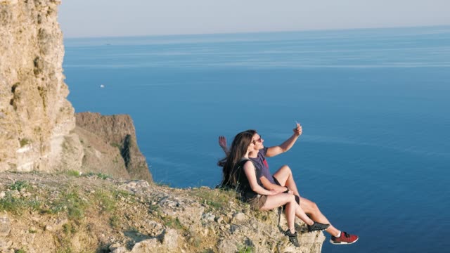 Side-view-active-tourist-couple-posing-taking-selfie-using-smartphone-on-edge-cliff-break