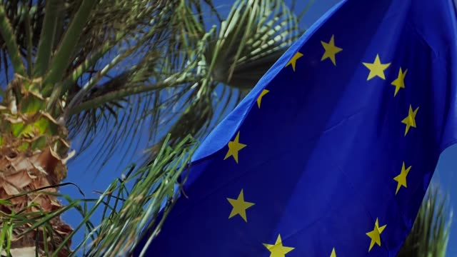 Ondeando-la-bandera-de-la-Unión-Europea-en-el-viento-con-un-cielo-azul.