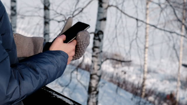 Mujer-de-primer-plano-las-manos-en-guantes-de-escribir-mensajes-en-el-teléfono-móvil-en-el-parque-de-invierno.