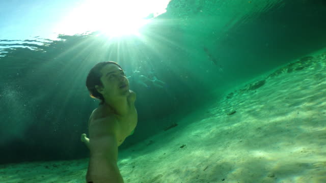 Vista-submarina-de-POV-de-joven-nadar-en-cristalinas-aguas-azules-tropicales-en-un-día-soleado-con-destello-de-lente