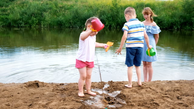 Little-children-play-in-the-river-in-the-summer,-a-girl-and-a-boy-are-building-a-stream.-Mom-looks-after-babies-during-a-walk