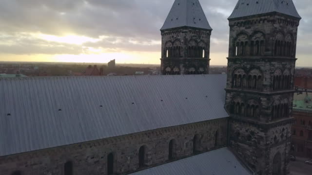 Drone-aéreo-Catedral-de-Lund-tiro.-Vuelo-siguiente-al-edificio-de-la-iglesia-y-Torres,-horizonte-de-la-ciudad-de-Lund-en-puesta-del-sol