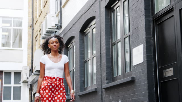 Modisch-junge-schwarze-Frau-rot-gepunkteten-Hosen-zu-Fuß-entlang-einer-Straße,-niedrigen-Winkel