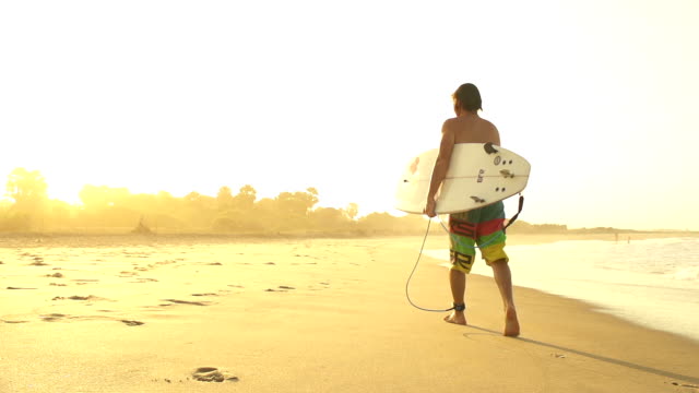 Surfer-walking-out-of-the-water-after-session-at-sunset