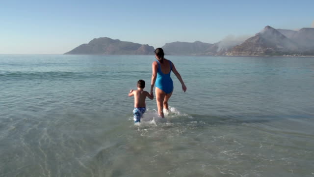 Mutter-und-junge-Jungen-spielen-im-seichten-Wasser-am-Strand,-Cape-Town