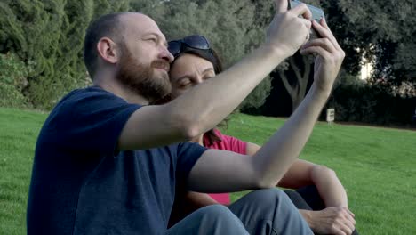 A-couple-takes-selfies-while-sitting-on-grass.-Quality-time-concept.