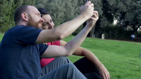 A-couple-takes-selfies-while-sitting-on-grass.-Quality-time-concept.