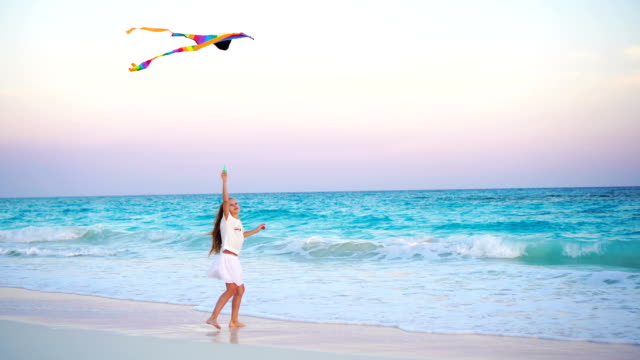 Adorable-little-girl-with-flying-kite-on-tropical-beach.-Kid-play-on-ocean-shore-with-beautiful-sunset