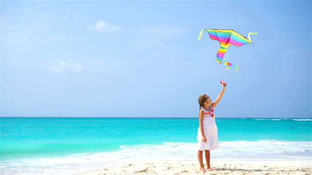 Little-girl-with-flying-kite-on-tropical-beach.-Kid-play-on-ocean-shore.-Child-with-beach-toys.