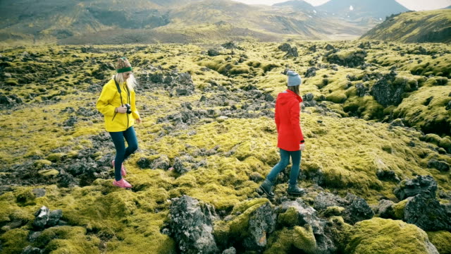Helicóptero-volando-a-alrededor-de-dos-mujeres-en-el-campo-de-lava-en-Islandia.-Turistas-con-cámara-en-la-naturaleza-y-tomar-fotografías