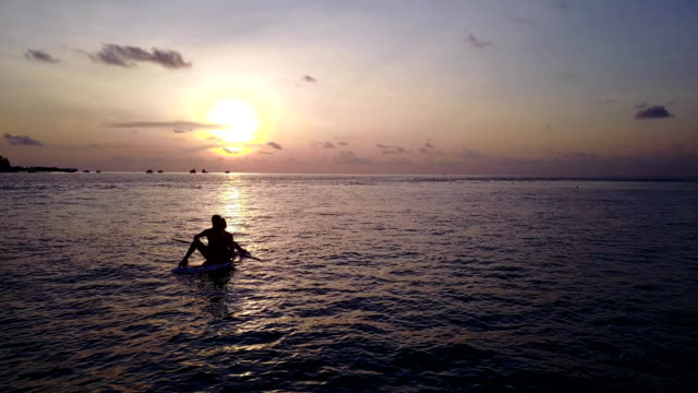 v04085-fliegenden-Drohne-Luftaufnahme-der-Malediven-weißen-Sandstrand-2-Personen-junges-Paar-Mann-Frau-Paddleboard-Rudern-Sonnenuntergang-Sonnenaufgang-auf-sonnigen-tropischen-Inselparadies-mit-Aqua-blau-Himmel-Meer-Wasser-Ozean-4k