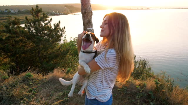 Young-attractive-woman-playing-with-a-dog-Jack-Russell-in-the-meadow-at-sunset-with-sea-background.-slow-motion