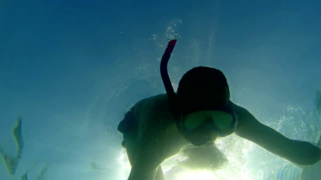 Ein-Taucher-bewegt-sich-langsam-unter-Wasser-mit-Sonnenstrahlen-Glanz-aus-Hintergrund